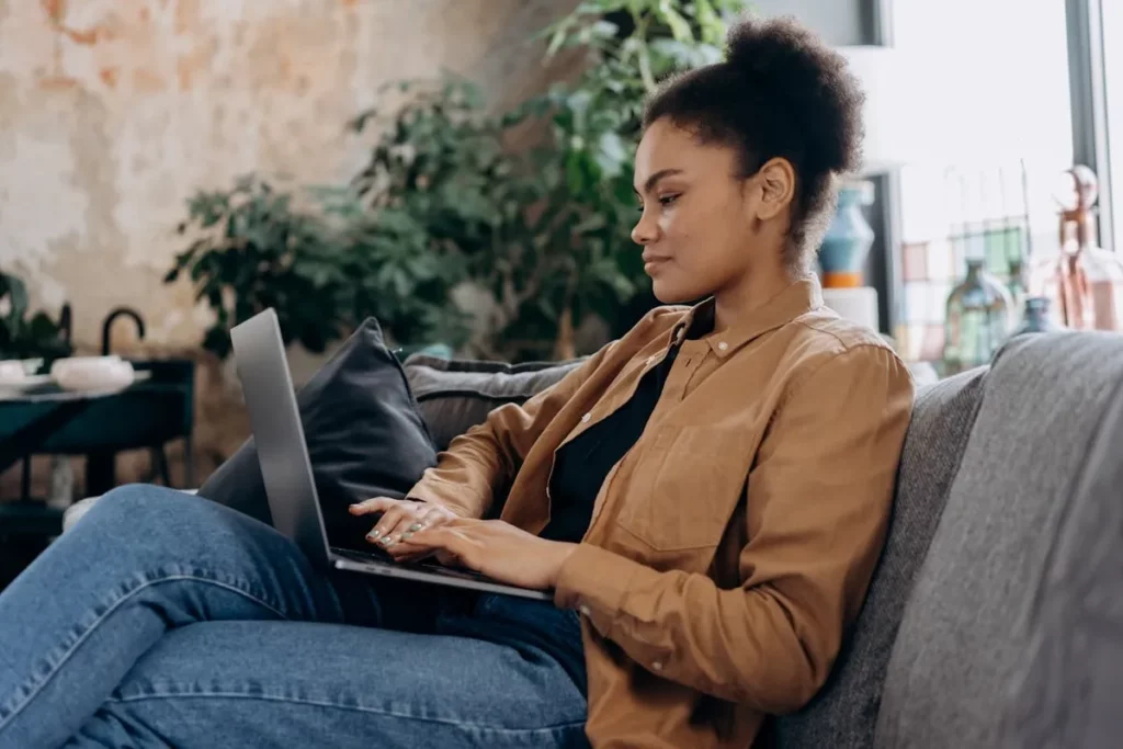 Mulher sentada no sofá usando notebook em ambiente aconchegante e bem iluminado