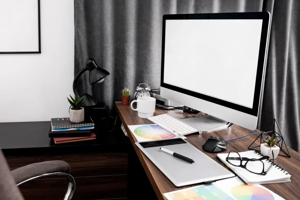 Imagem de uma área de trabalho moderna e bem organizada, com computador, livros, plantas, caneta e materiais de design sobre a mesa