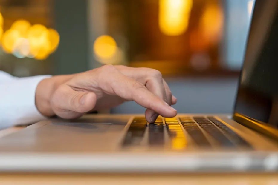 Mão de uma pessoa digitando em um teclado de laptop, com fundo suave e iluminado