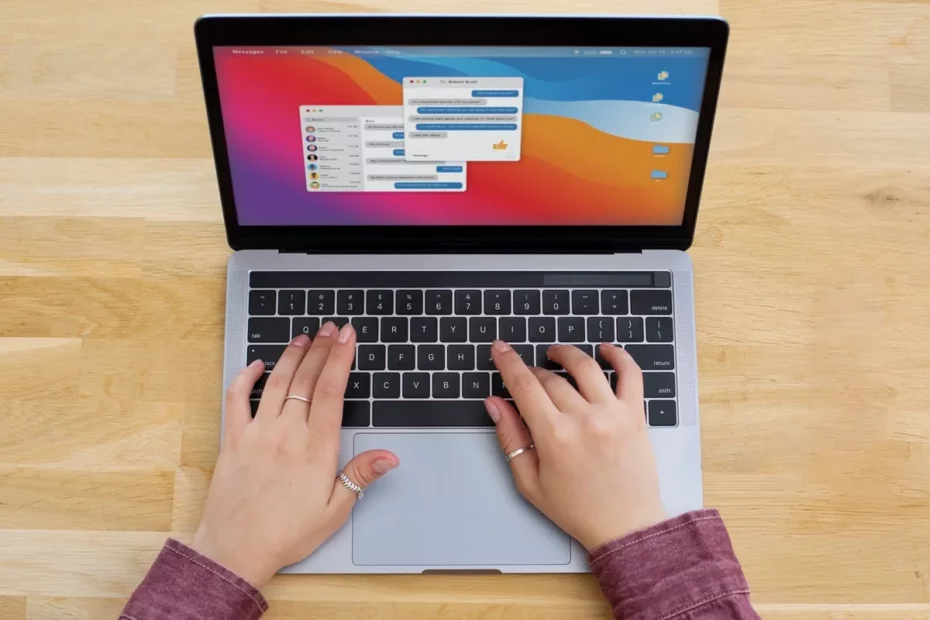 Mulher digitando no teclado de um MacBook com janelas de mensagens abertas na tela