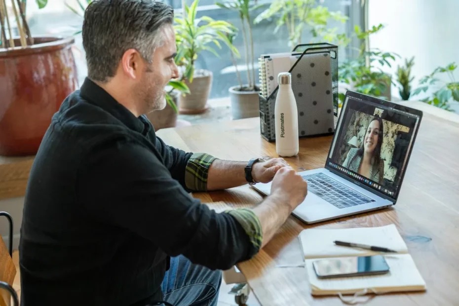 Homem de cabelos grisalhos participando de entrevista de emprego online em notebook, sorrindo para uma mulher na chamada de vídeo
