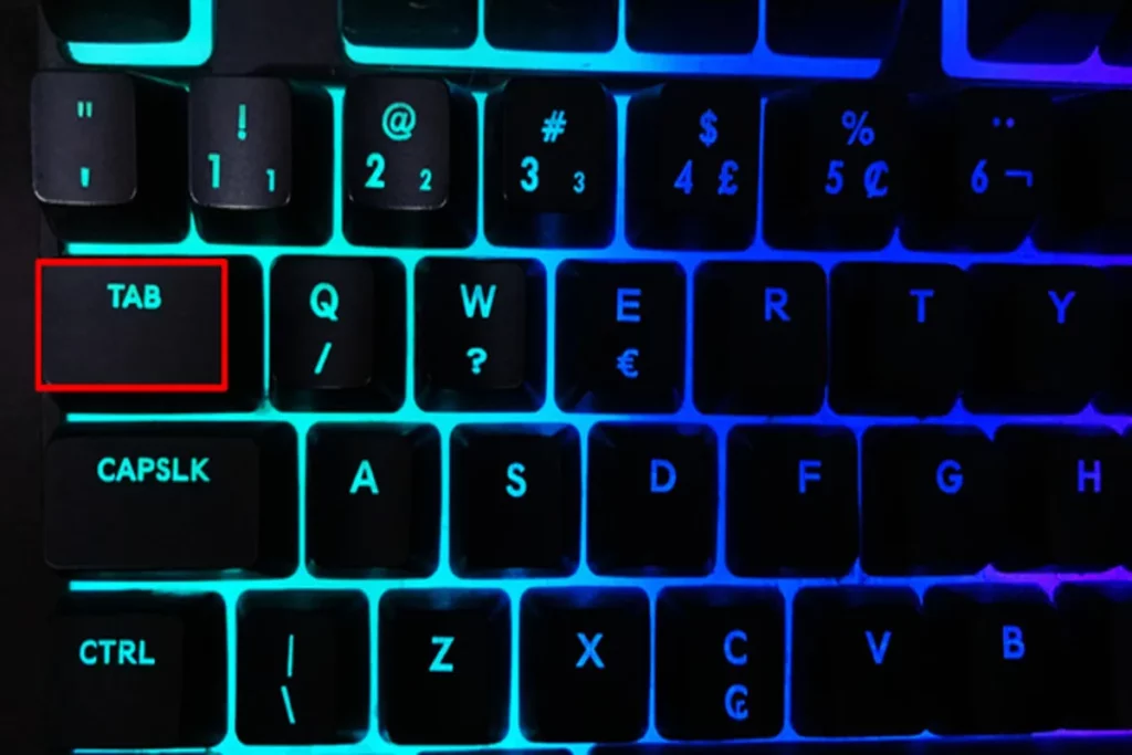 Tecla TAB destacada em vermelho em teclado iluminado com luz azul, ao lado da tecla Q