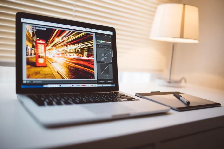 Laptop moderno em uma mesa de trabalho, com um software de edição de imagem aberto e uma lâmpada ao fundo. Imagem relevante para como diminuir o brilho da tela e ergonomia.
