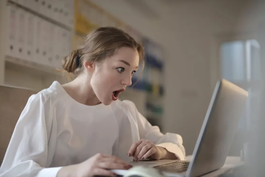 Mulher chocada olhando para a tela de um laptop, expressando a surpresa e o desapontamento quando o computador não liga.