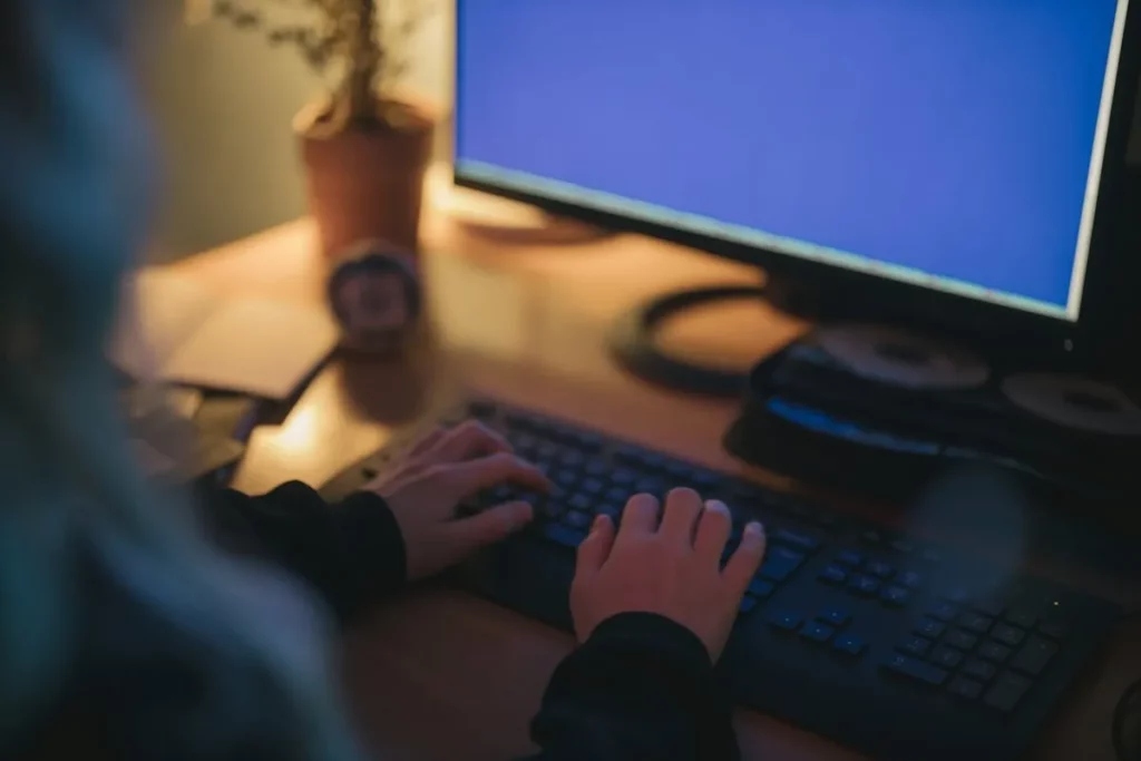 Pessoa digitando no computador, má postura, possível dor no pescoço, trabalho remoto.