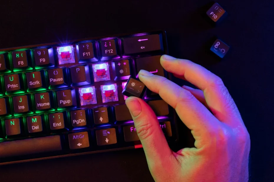 Close-up de uma mão removendo ou encaixando uma keycap (tecla) em um teclado mecânico gamer RGB com switches visíveis e iluminação verde e roxa, representando a personalização.