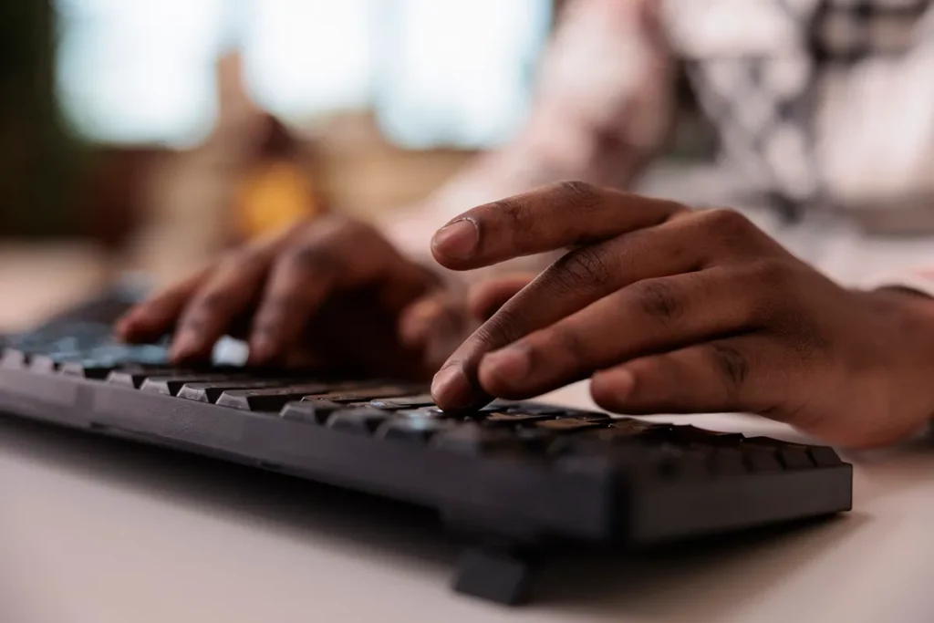Mãos de uma pessoa digitando em um teclado de computador em um ambiente de trabalho.