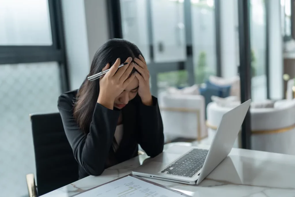 Mulher de frente para laptop, com as duas mãos na cabeça.