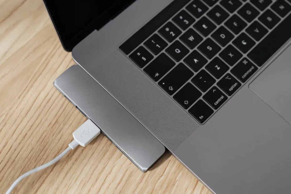 hub usb metálico conectado na lateral de um notebook sobre mesa de madeira com cabo usb plugado