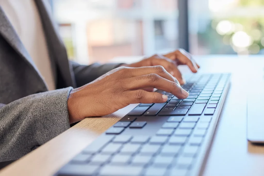 Mãos digitando em teclado de perfil baixo sobre mesa de madeira em ambiente iluminado