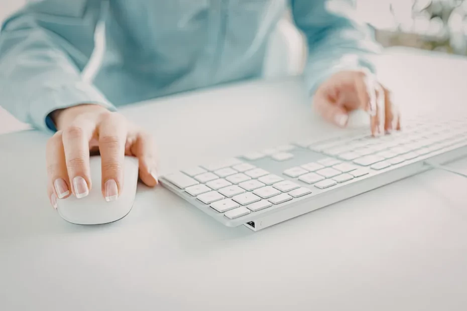 Mão usando mouse ao lado de teclado branco em mesa limpa durante uso do computador