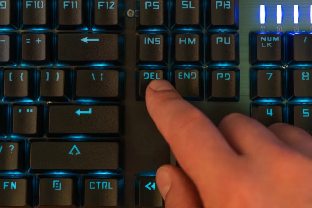 dedo pressionando a tecla Del em teclado iluminado de computador
