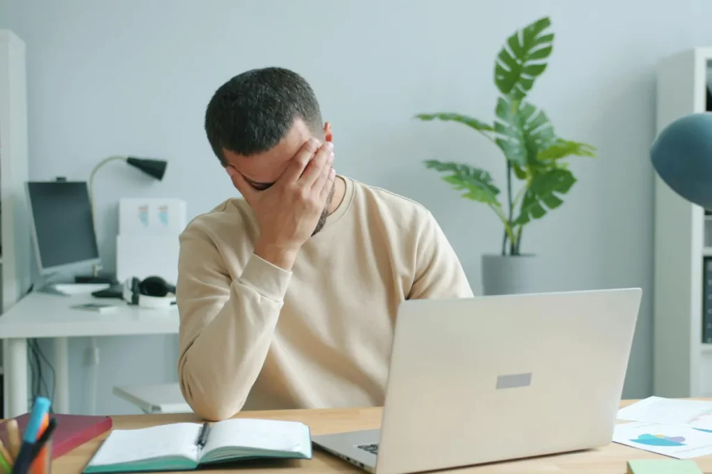 homem usando notebook com expressão de dúvida e mãos abertas como sinal de confusão