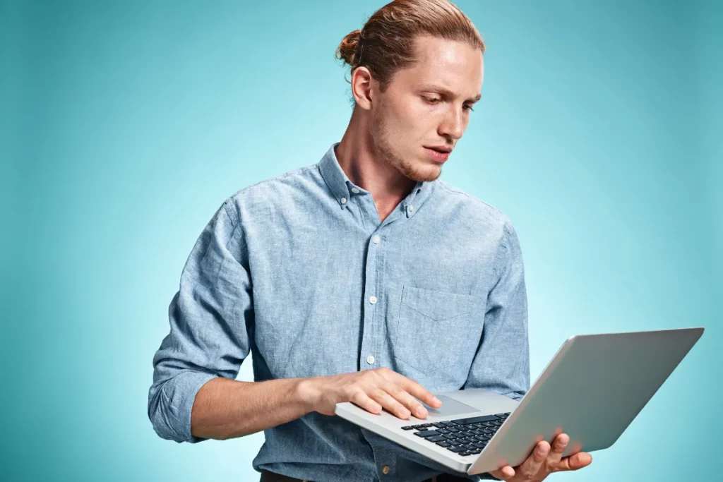 homem segurando notebook e tentando usar o teclado com expressão de preocupação
